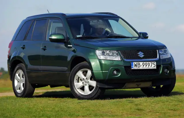 Zielony Suzuki Grand Vitara 2 na tle błękitnego nieba i zielonej trawy.