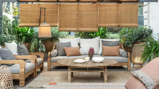 Acogedora terraza estilo mediterráneo con sofá, sillones de madera, mesa de centro y abundante vegetación.
