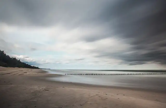 Spokojna plaża i morze, idealne na wypoczynek w ośrodku wczasowym Zacisze. Długie fale i las sosnowy tworzą malowniczy krajobraz.