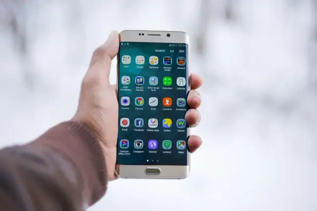 Dłoń trzymająca złoty telefon Samsung z ikonami aplikacji na ekranie.