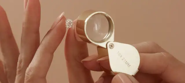 Eine Hand hält einen funkelnden Diamanten, während eine Lupe ihn vergrößert. Ein perfekter einschluss diamant wird genau geprüft.