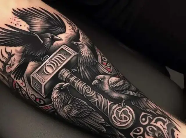 Tatuaż kruka z młotem Thora. Kruki symbolizują mądrość i pamięć, a młot to potęga i ochrona.