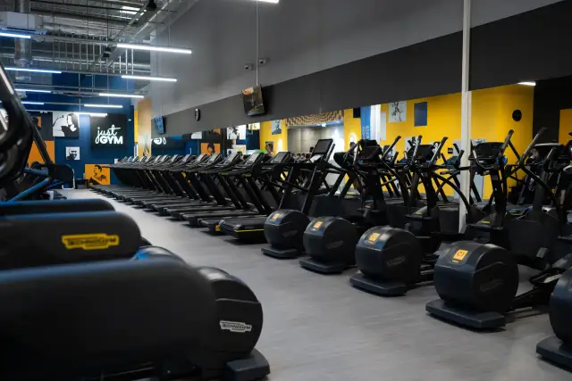 Rzędy bieżni i orbitreków w siłowni Just Gym. Chcesz wiedzieć, jak wejść na Multisport? Tu zaczynasz trening!