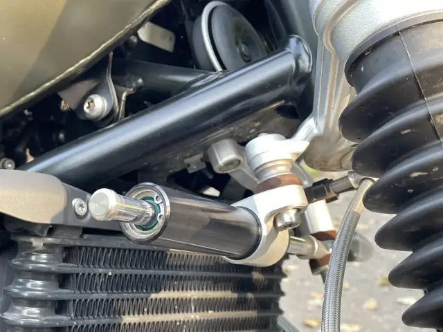 Amortyzator skrętu motocykl, zamontowany obok chłodnicy, zapewnia stabilność kierownicy podczas jazdy.