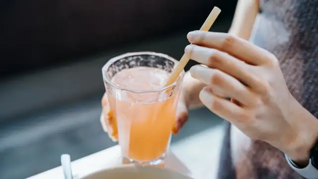 Glas mit rosafarbenem Getränk und Eis, eine Hand hält einen Strohhalm. Vielleicht ein gesunder Drink mit Sauerkrautsaft Inhaltsstoffe.