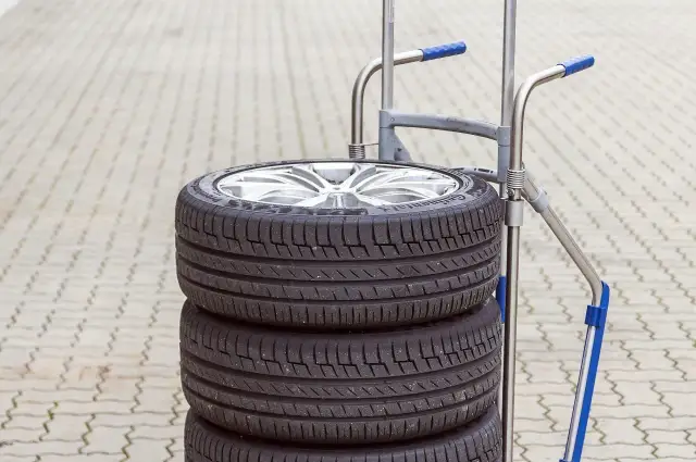 Stos czterech opon samochodowych na wózku. Zastanawiasz się, ile waży opona samochodowa? Ten zestaw jest gotowy do transportu.