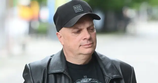 Krzysztof Skiba w czarnej czapce z napisem "BRK LYN" i skórzanej kurtce, zamyślony.