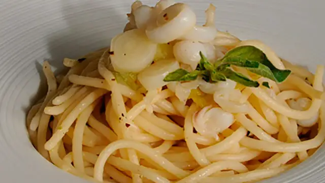 Deliciosos espaguetis con calamares, un plato de pasta con trozos de calamar y hojas verdes, servido en un cuenco blanco.