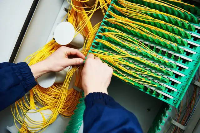 Mains de technicien travaillant sur un panneau de brassage fibre optique, gérant un câble fibre cassé.