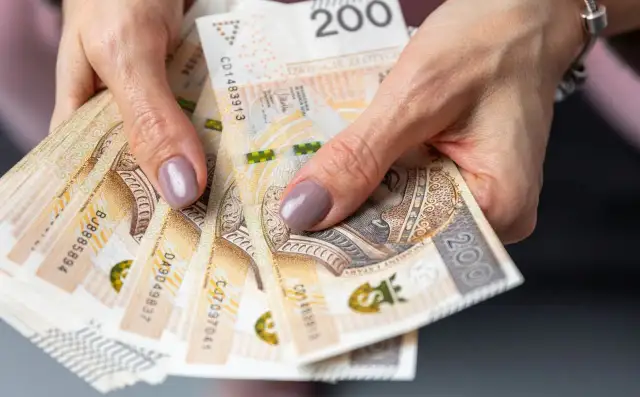 Dłonie trzymające stos banknotów 200 zł. Pieniądze mogą symbolizować oszczędności na przyszłość, np. na okresową emeryturę kapitałową.