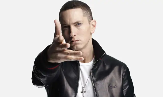Eminem w czarnej kurtce i białej koszulce, gestykuluje ręką.