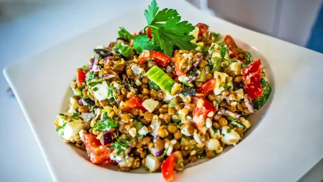 Ein bunter Linsensalat mit Feta, Tomaten, Gurken und frischer Petersilie, garniert mit einem Petersilienblatt.
