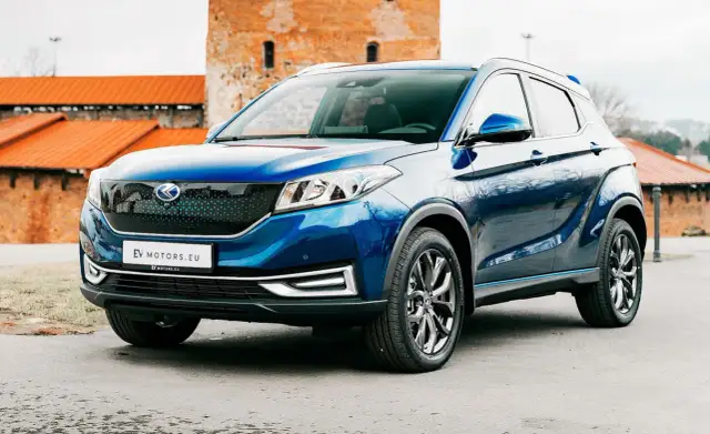 Błękitny SUV EV Motors.eu na tle ceglanych budowli. Jego nowoczesny design i ekologiczne serce przyciągają wzrok.