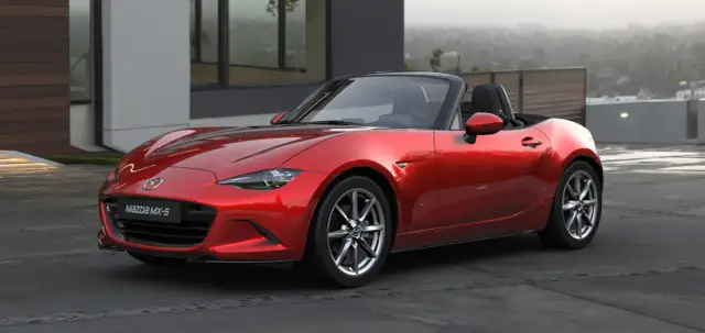 Czerwone Mazda MX-5, jedne z najbardziej pożądanych aut sportowych, lśni na tle nowoczesnej architektury.