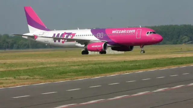 Samolot Wizz Air z różowym kadłubem i fioletowym ogonem na pasie startowym.