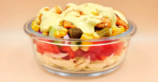 Sałatka gyros w szklanej misce z kurczakiem, kukurydzą, ogórkiem i sosem.