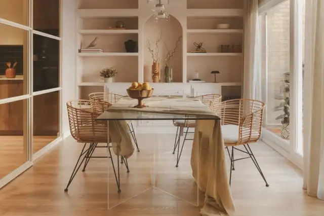 Comedor moderno con mesa de cristal y sillas de ratán. Estanterías empotradas con decoración. El precio del proyecto de interiorismo se ajusta a este estilo.