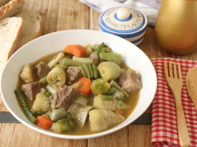 Un reconfortante plato de menestra de ternera con trozos de carne tierna y verduras como alcachofas, judías verdes y zanahorias.