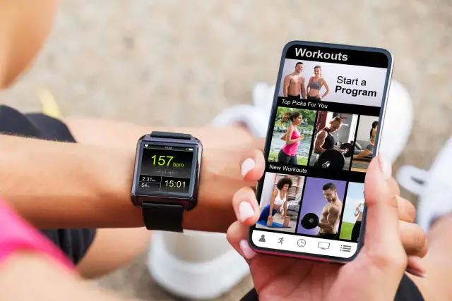 Une personne utilise son smartphone pour apprendre comment régler une montre connectée smartwatch, affichant des entraînements et des données de fitness.