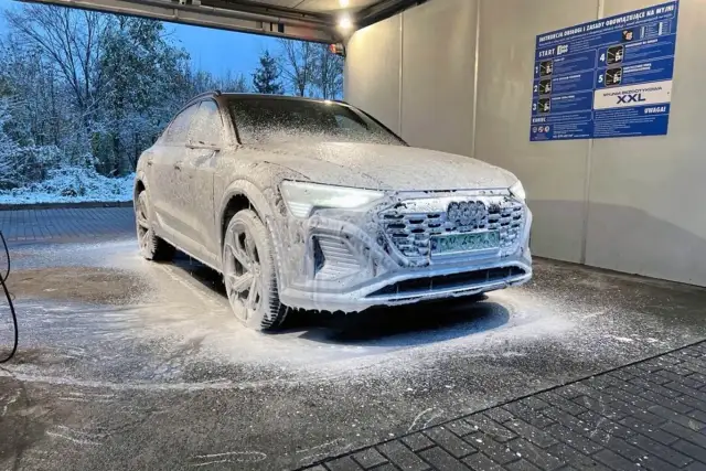 Audi pokryte pianą na myjni bezdotykowej zimą. Śnieg na drzewach w tle.