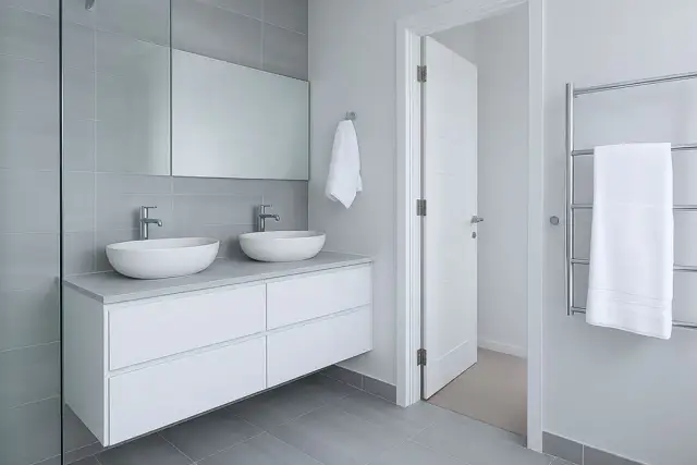 Modernos lavabos dobles sobre mueble blanco, espejo grande y azulejos grises. ¡Ideas para reformas de baños elegantes y funcionales!