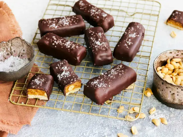 Vegane Snickers mit Karamell, Erdnüssen und Meersalz bestreut, auf einem goldenen Gitter.