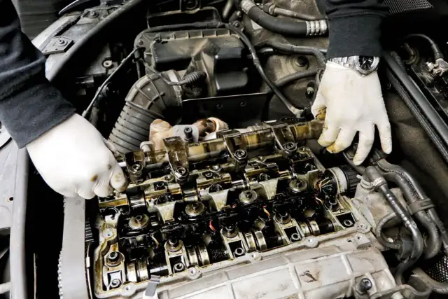 Mechanik w białych rękawiczkach sprawdza stan wytartego wałka rozrządu w silniku samochodowym.