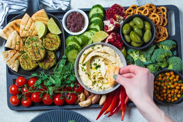 Taca z przekąskami na ognisko: hummus, falafel, warzywa, owoce, pieczywo i paluszki.