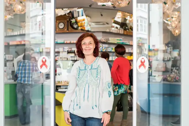 Frau lächelt vor einer Apotheke mit roten Aids-Schleifen am Eingang.