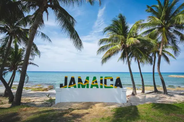 Napis "JAMAICA" na tle plaży, morza i palm.