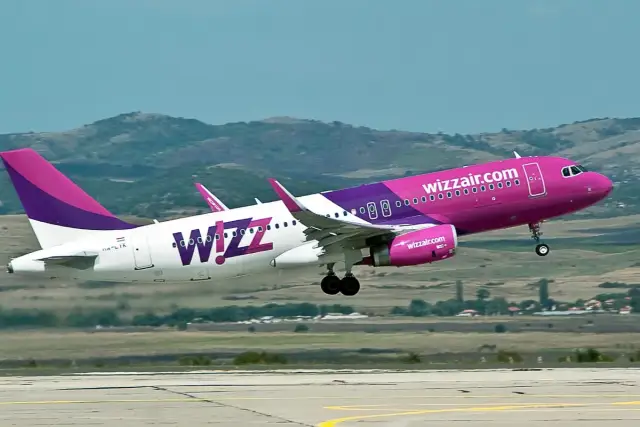Dwa samoloty Wizz Air z różowymi i fioletowymi elementami startują na tle wzgórz.
