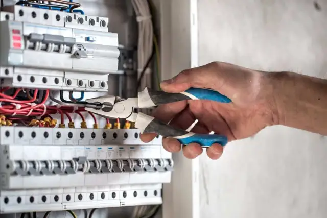 Elektryk z kombinerkami przy skrzynce z bezpiecznikami, przygotowuje się, jak włączyć prąd.