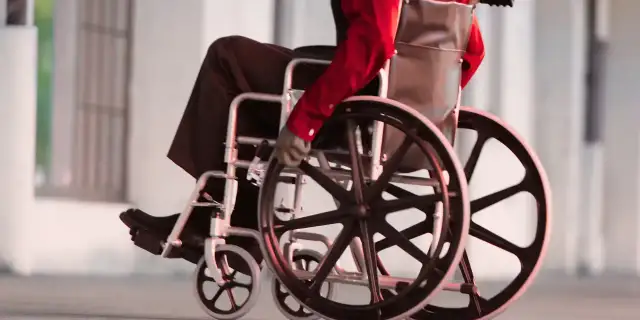 Osoba na wózku inwalidzkim w czerwonej koszuli i czarnych spodniach porusza się po chodniku.