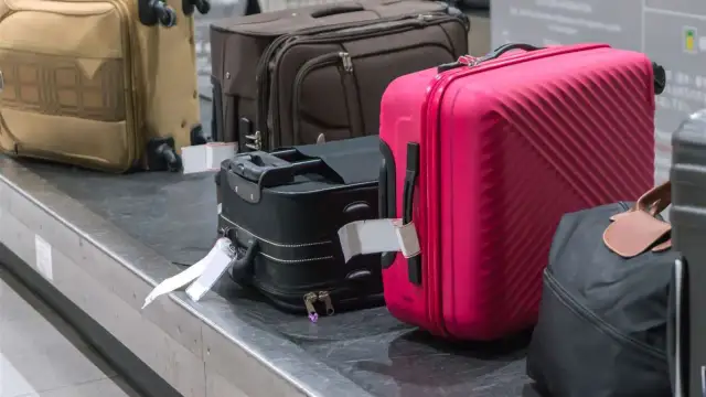 Suitcases on a baggage carousel, including a bright pink one.