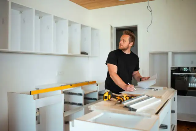 Mężczyzna planuje, jak zabudować przestrzeń nad szafkami kuchennymi, analizując projekt.