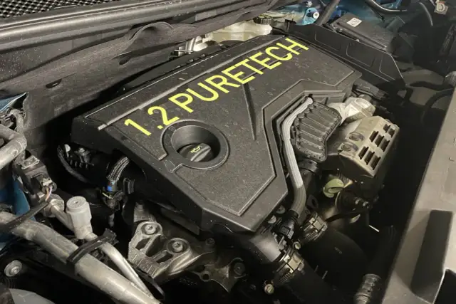 Silnik 1.2 PureTech, często chwalony w opiniach za oszczędność. Widok z bliska na pokrywę silnika z żółtym napisem.