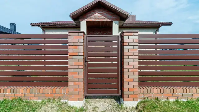 Eleganckie ogrodzenie z klinkieru i brązowych paneli, z solidną bramą wjazdową, stanowi ozdobę posesji.