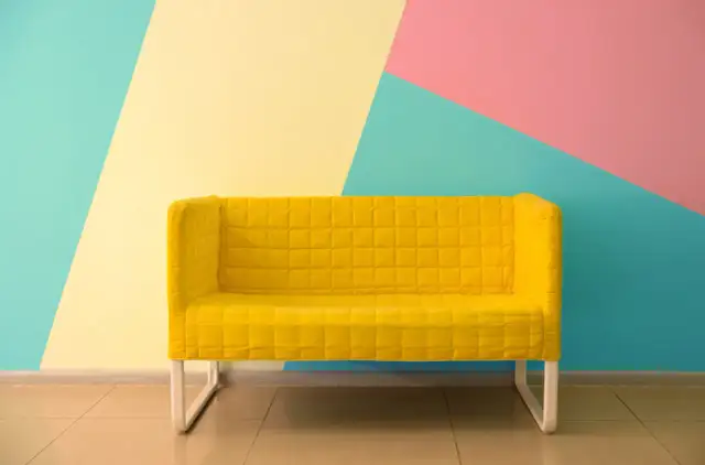 Żółta kanapa na tle geometrycznej ściany w kolorach: miętowym, żółtym i różowym. Świetne inspiracje jak pomalować pokój!
