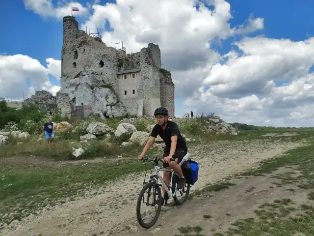 Młody mężczyzna na rowerze przemierza malowniczą trasę po Jurze Krakowsko-Częstochowskiej, mijając ruiny zamku.