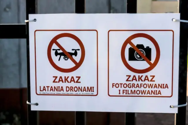 Dwa znaki na płocie: zakaz latania dronami i zakaz fotografowania i filmowania.