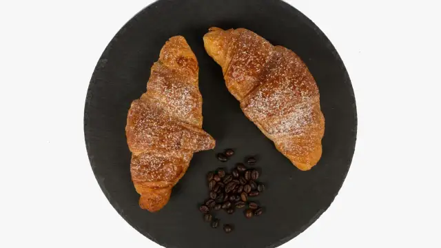 Dos cruasanes dorados espolvoreados con azúcar glas, junto a granos de café. Una delicia para aprender como hacer cruasanes.
