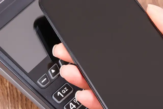 Zbliżenie na dłoń trzymającą telefon nad terminalem płatniczym. Szybki sposób, jak doladowac telefon Play.