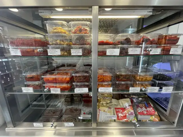 Witryna chłodnicza z różnymi rodzajami kimchi i koreańskich przekąsek w plastikowych pojemnikach.