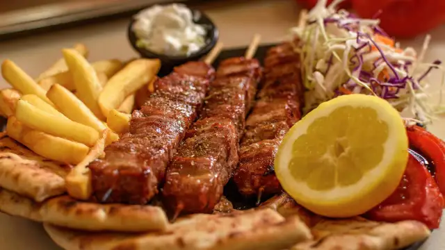 Pyszne souvlaki na patykach, podane z frytkami, pitą, sałatką i cytryną.