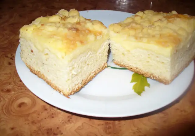 Puszyste ciasto drożdżowe z serem, z kruszonką na wierzchu, pokrojone na dwa kawałki na białym talerzu.