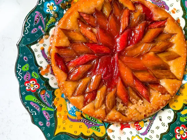 Owoce pod kruszonką, czyli tarta tatin z rabarbarem, błyszcząca od karmelu, na kolorowym, zdobionym talerzu.