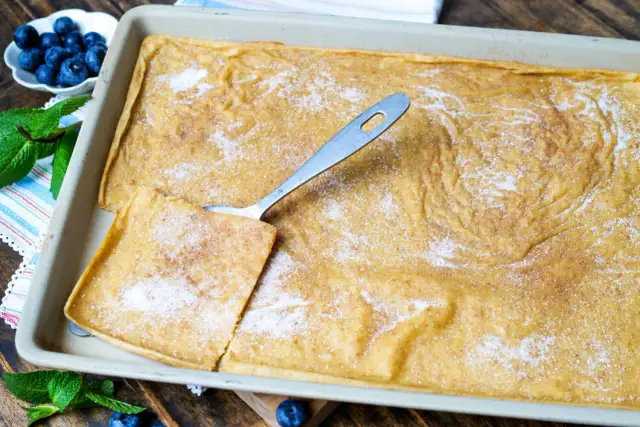 Ein frisch gebackener Ofenpfannkuchen, bestreut mit Zucker und Zimt, wartet darauf, serviert zu werden. Ein Stück ist bereits herausgeschnitten.