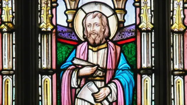 Witraż przedstawia świętego Łukasza z księgą i zwojem, symbolizując jego rolę jako ewangelisty i pisarza.
