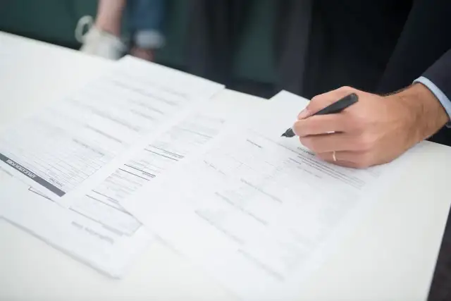 Ręka klienta podpisuje dokumenty ubezpieczeniowe. Agent ubezpieczeniowy czeka na zakończenie formalności.