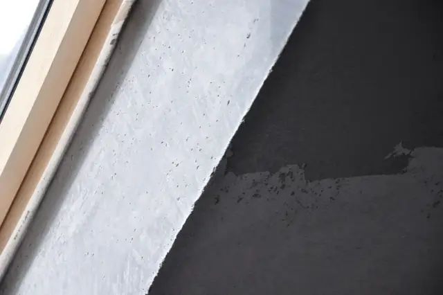 Fragment ściany z betonem architektonicznym i drewnianą ramą okienną. Zastanawiasz się, jak usunąć beton architektoniczny ze ściany?